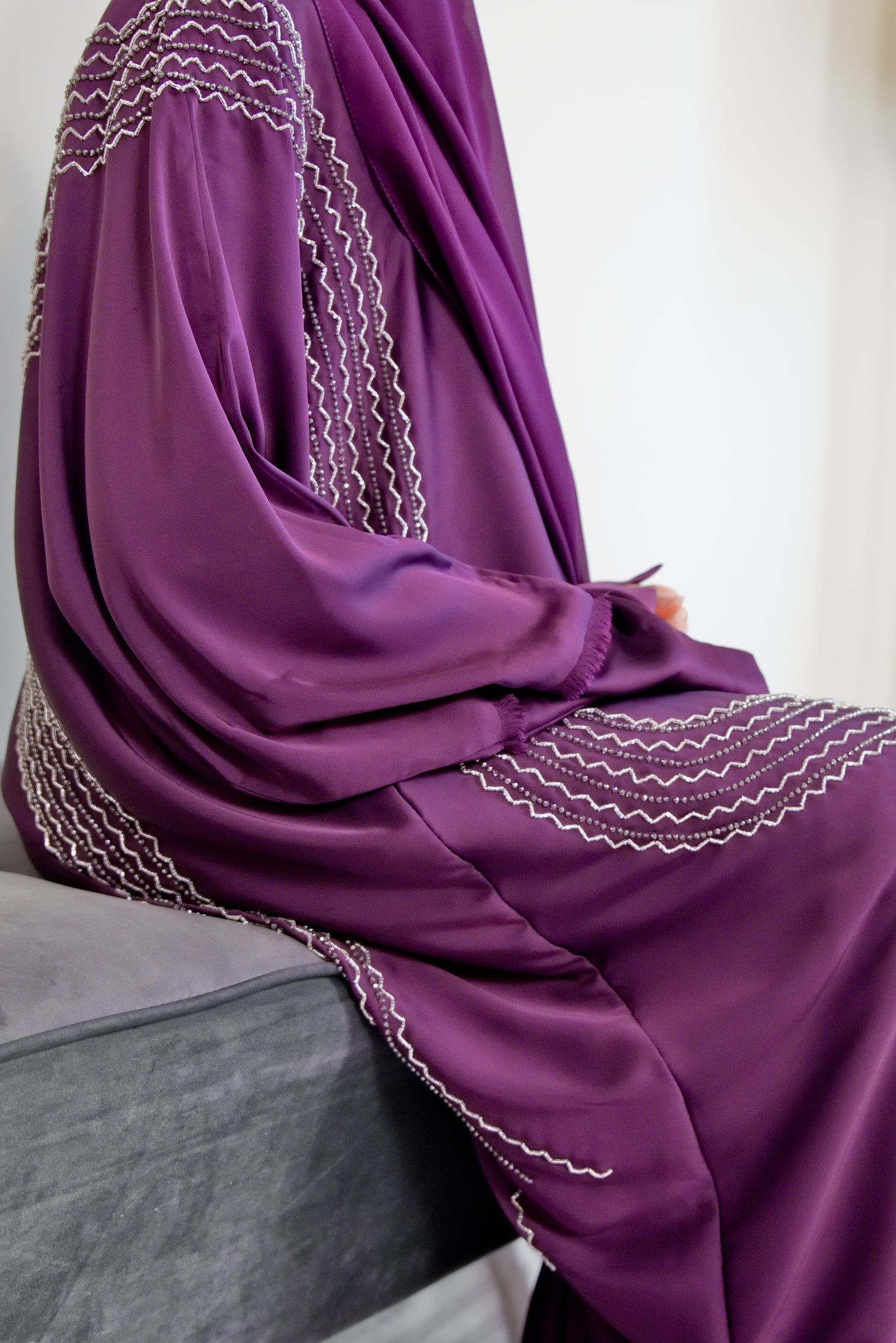 A person wearing a dark purple satin silk abaya with buttons at the front and handwork on the front and back, with matching chiffon hijab.