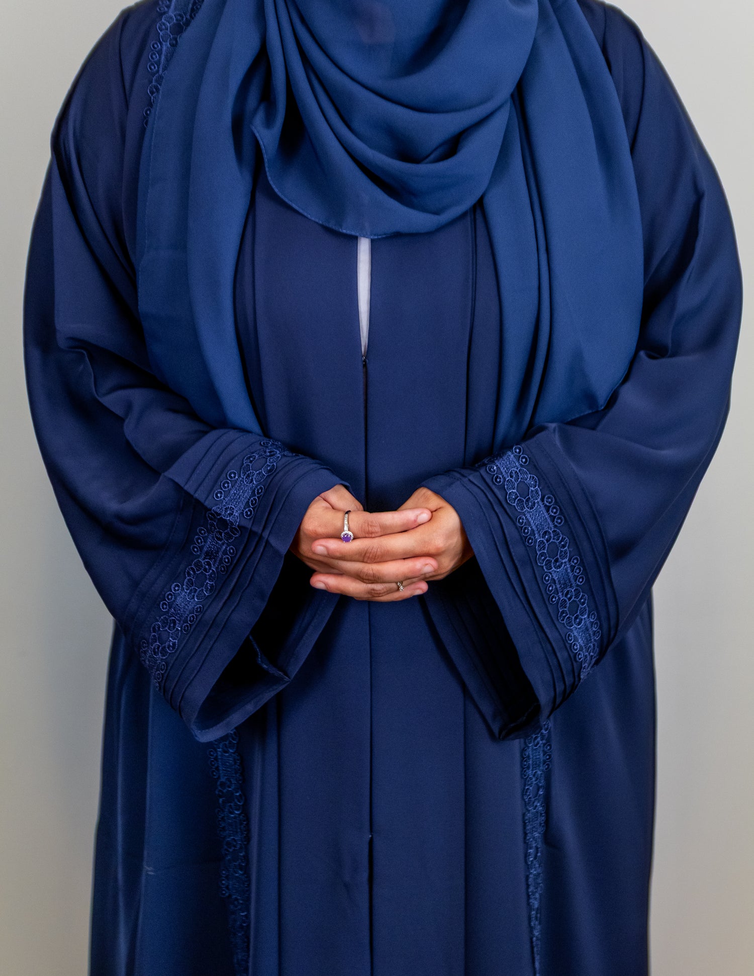 Person wearing a blue abaya with intricate designs on a plain background