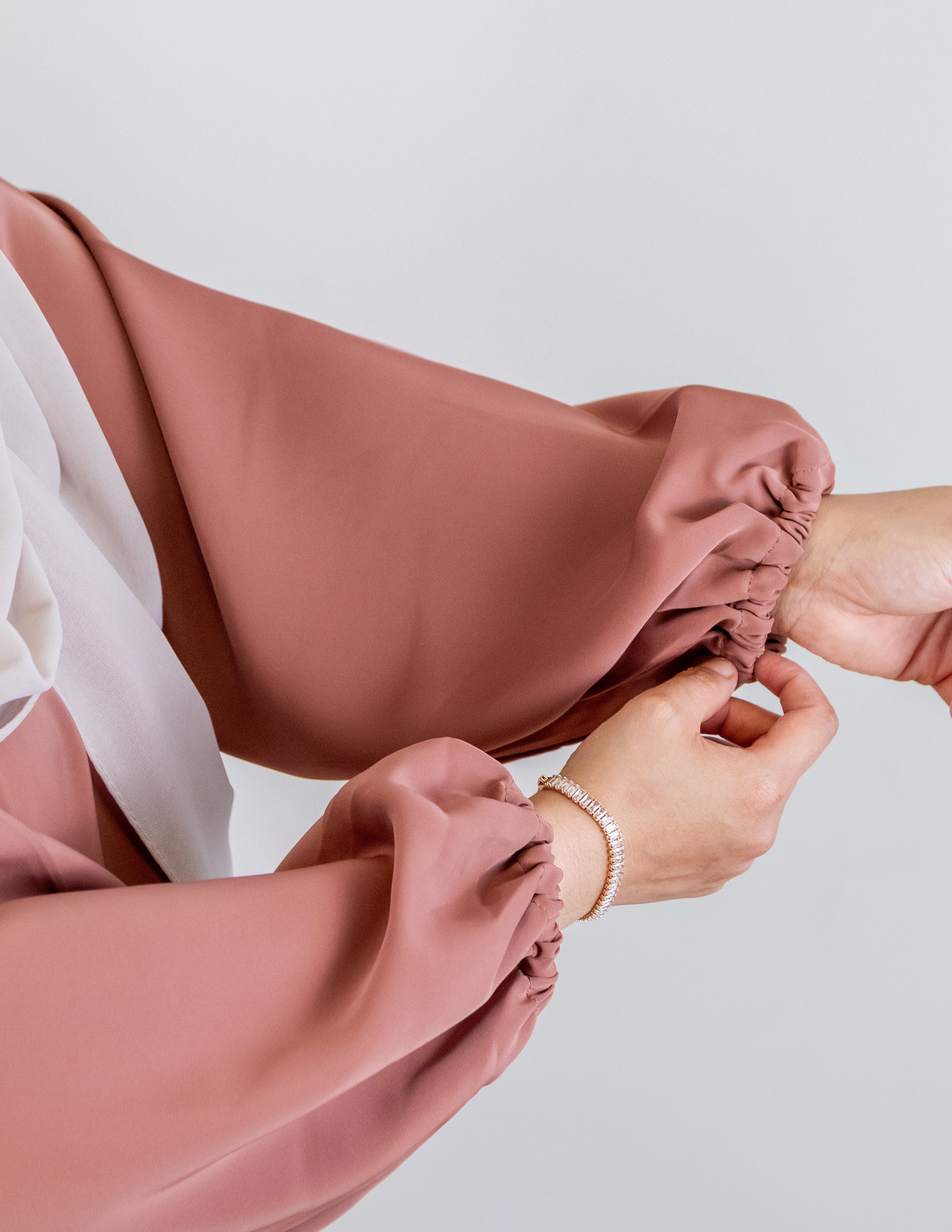 Person wearing a pink dress with long sleeves against a light gray background